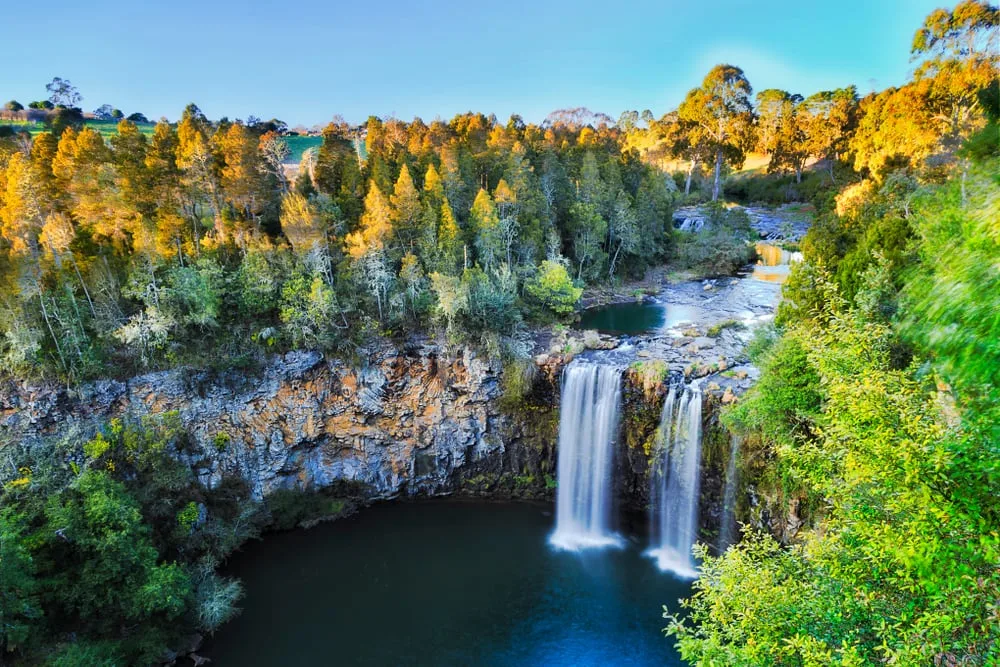 A scenic view of a wide waterfall plunging into a dark pool below a rugged cliff