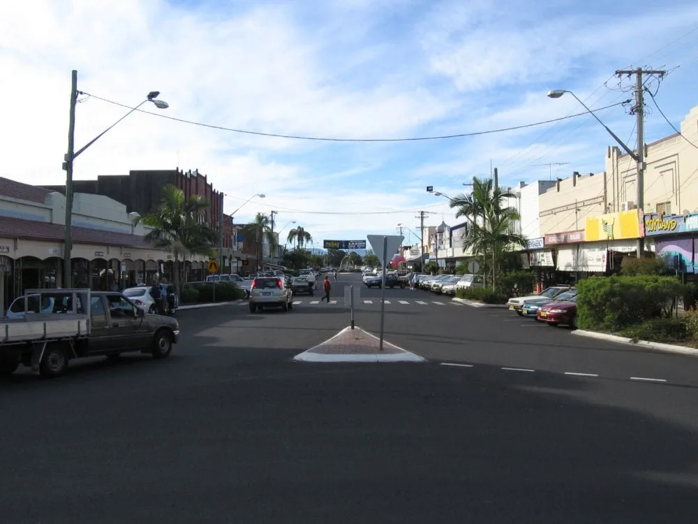 A town street lined with storefronts, palm trees, and parked vehicles