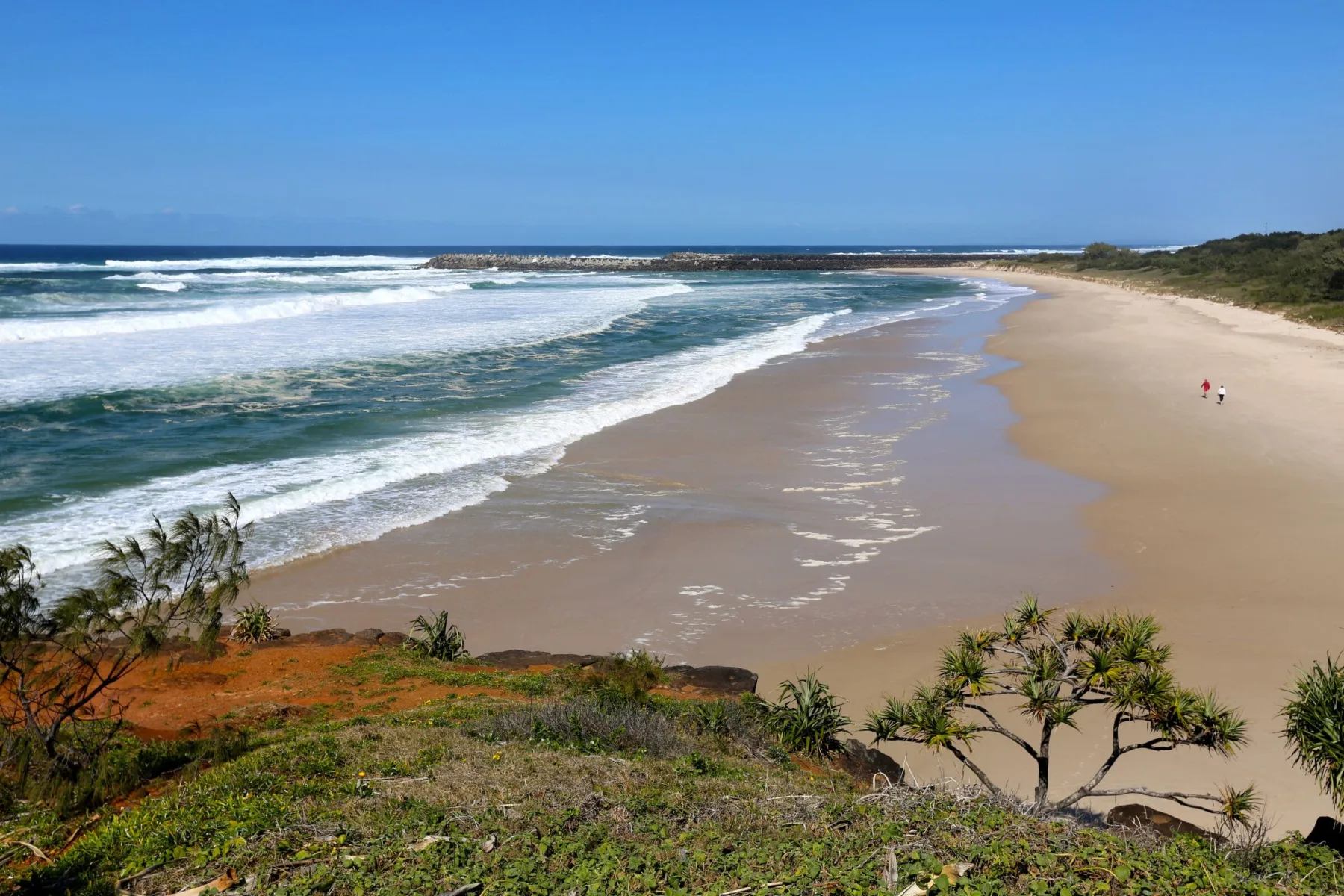 An elevated view looking down at a wide, sandy beach with ocean waves breaking on the shore.