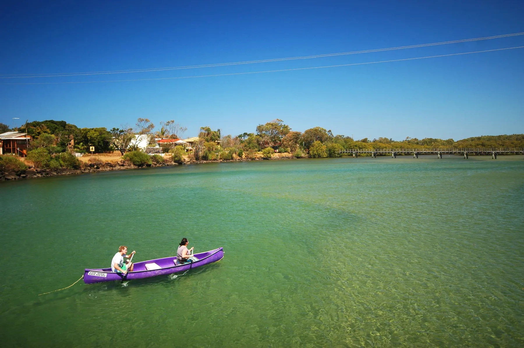 Two people paddle a bright purple canoe across a clear, turquoise river.