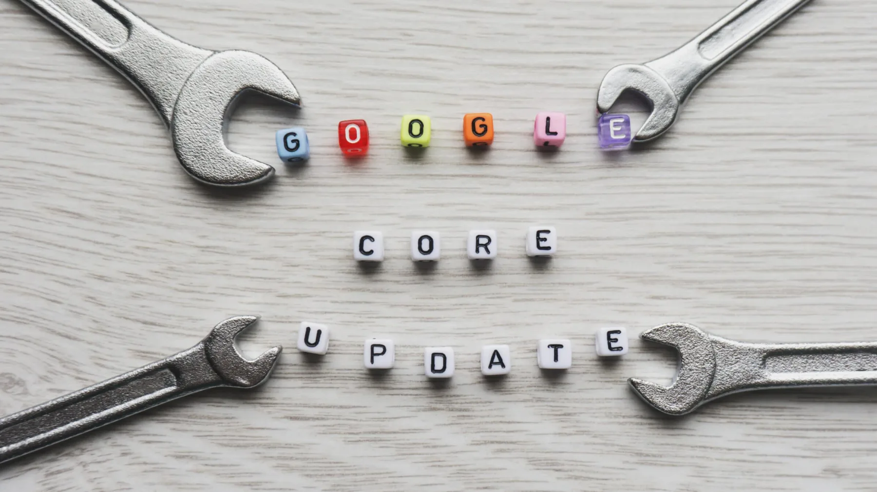 Small alphabet blocks spell out 'GOOGLE CORE UPDATE' on a light wooden surface, with colourful beads used for the word 'Google.