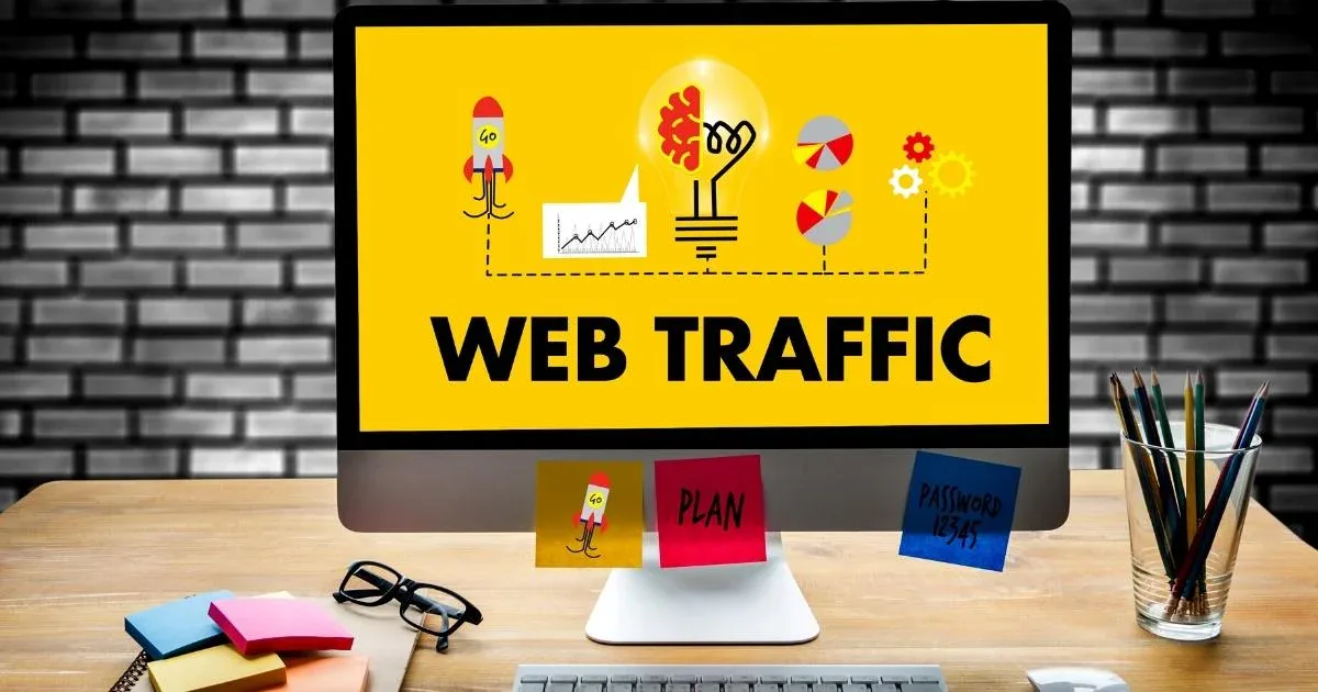 A desktop monitor displays a vibrant yellow screen with the bold text 'WEB TRAFFIC' accompanied by digital marketing icons like a rocket ship.