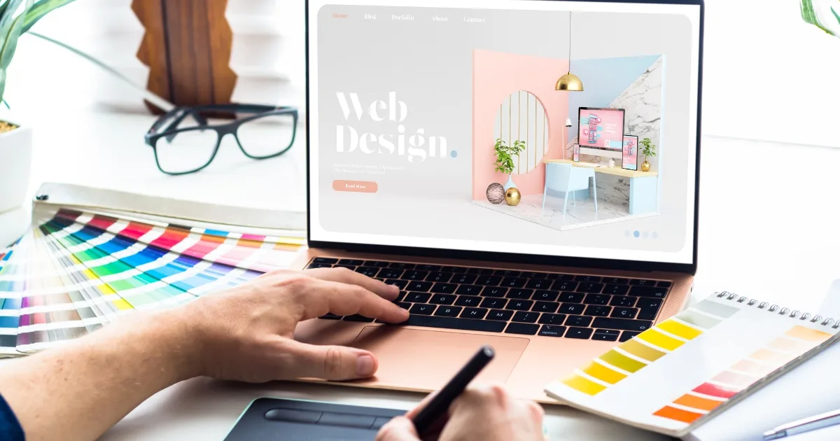 A designer's hands working on a laptop that displays a modern 'Web Design' portfolio page.