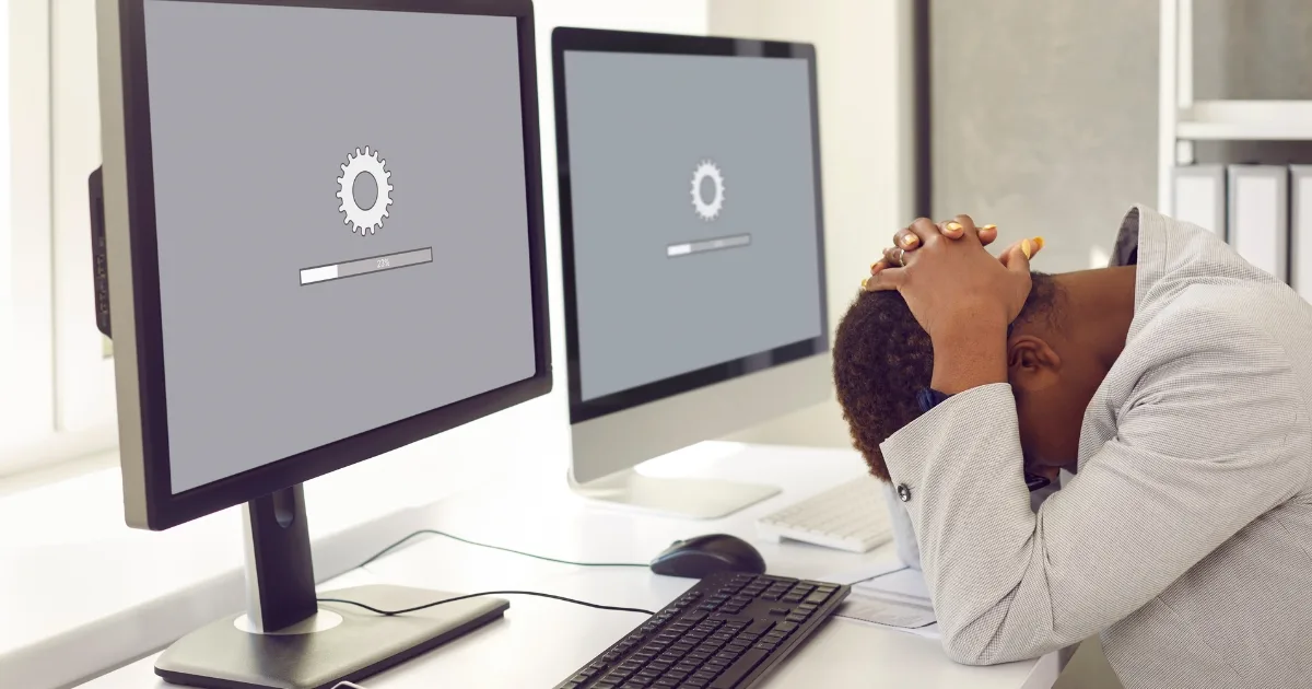 A person in a professional suit sits at a desk with their head in their hands