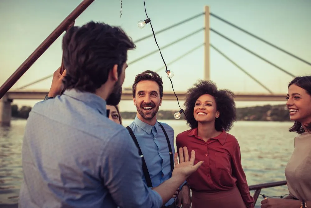 A group of four smiling friends talking outdoors on a boat or pier at sunset.