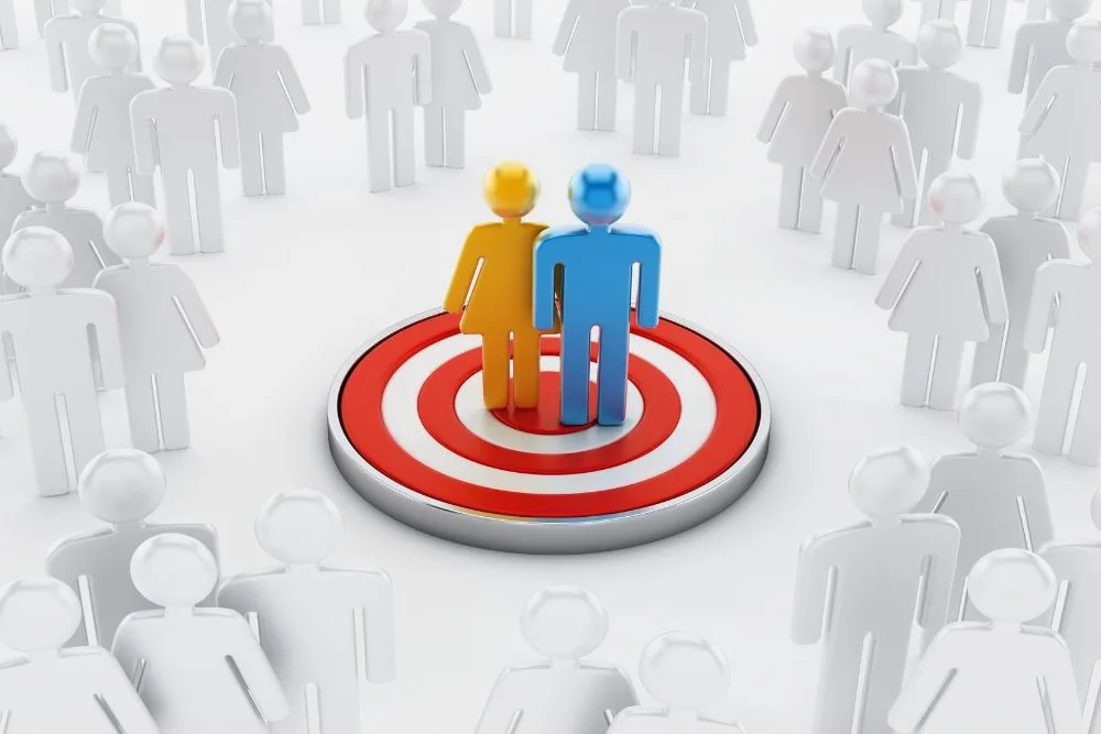 A 3D illustration of a yellow female figure and a blue male figure standing together on the centre of a red-and-white bullseye target.