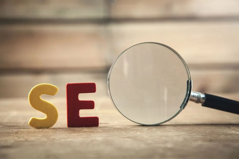 A close-up shot on a wooden surface featuring a yellow letter "S" and a red letter "E" next to a magnifying glass that acts as the "O" to spell out "SEO."