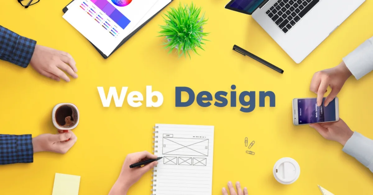 An overhead view of a creative team collaborating at a bright yellow desk with the words 'Web Design' in the centre