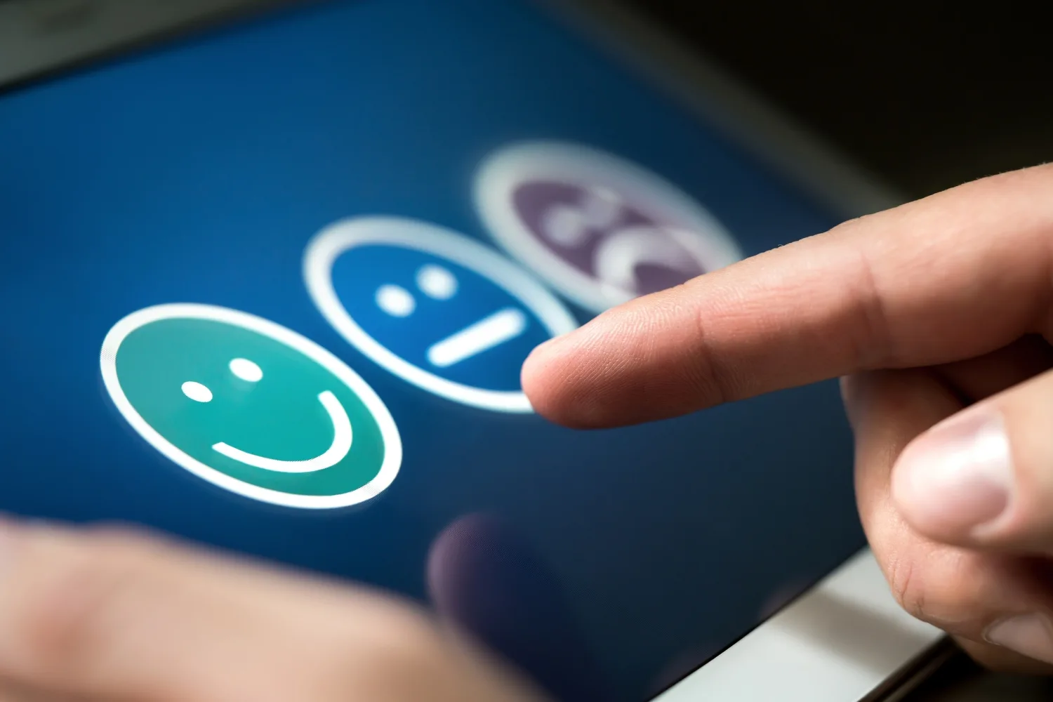 A person providing feedback on a tablet, selecting one of three smiley faces