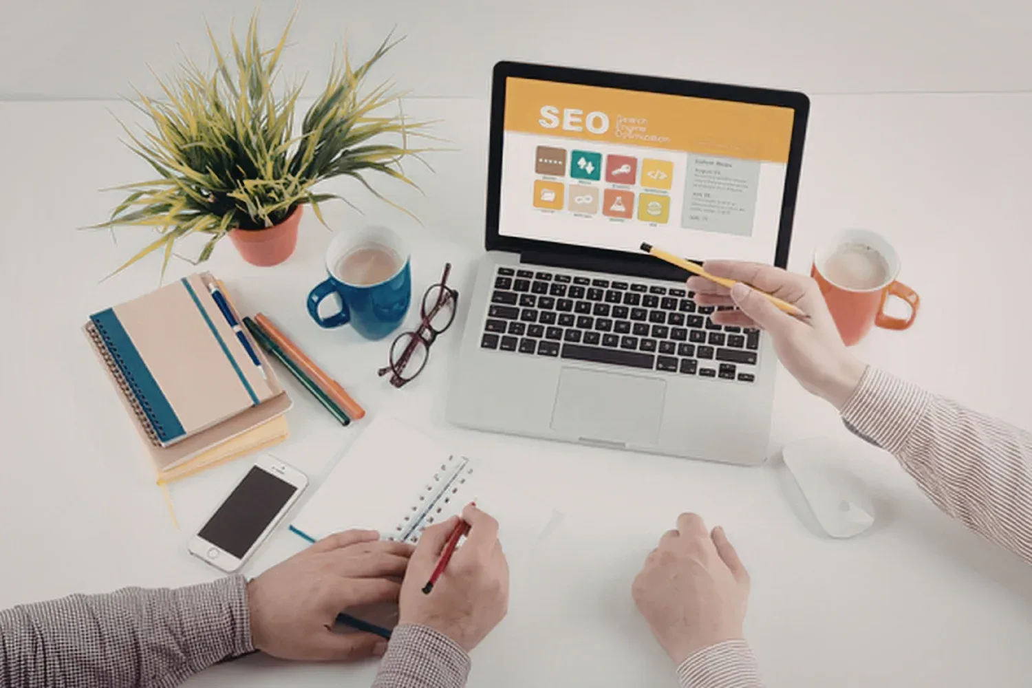 A desk where a person points a pencil at a laptop screen displaying an SEO diagram created from WordPress.