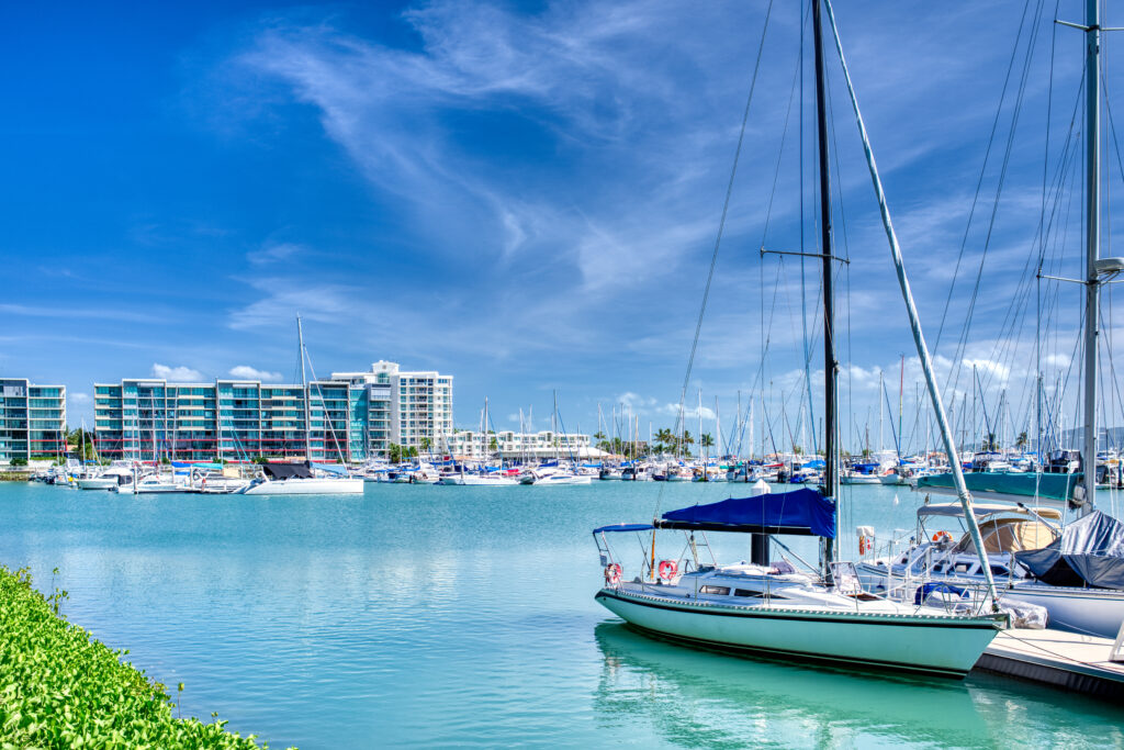A bright, scenic view of a luxury marina features several white sailboats and yachts moored in calm, turquoise water.