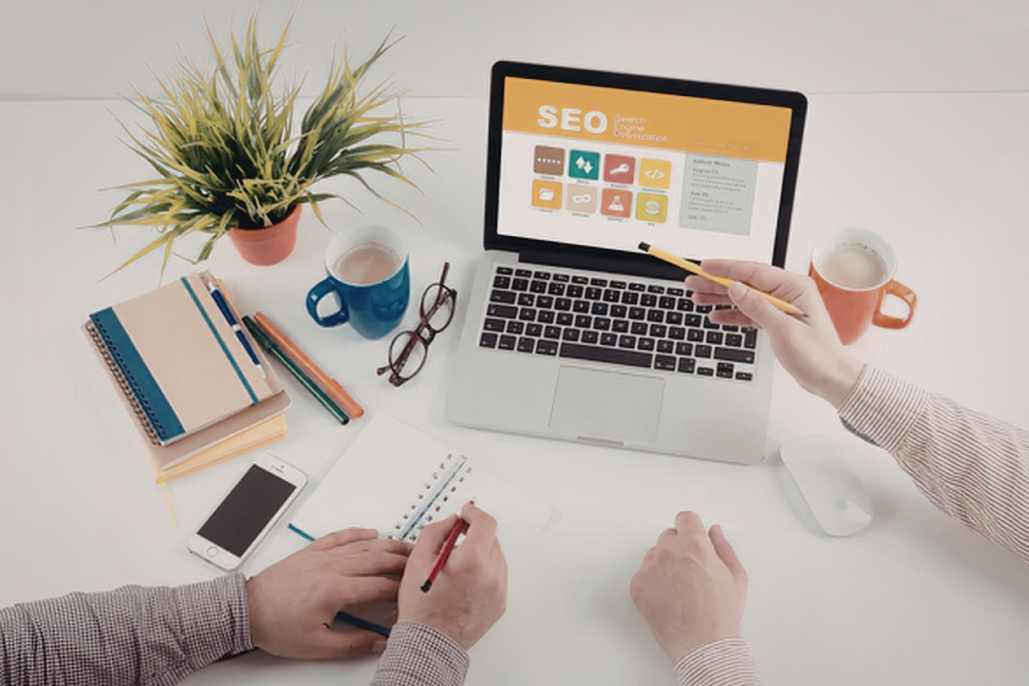 A desk where a person points a pencil at a laptop screen displaying an SEO diagram created from WordPress.